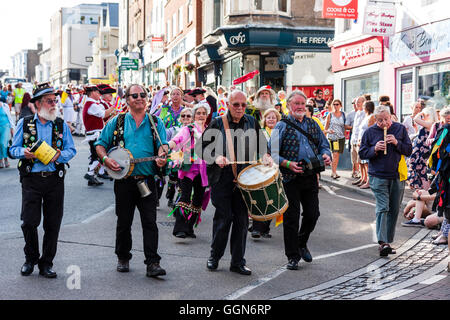 Festival de la semaine folklorique de Broadstairs. Parade. Quatre musiciens et mature, senior hommes jouant différents instruments, marcher le long de High Street, les gens sur l'observation de la chaussée. Venant vers viewer. Banque D'Images