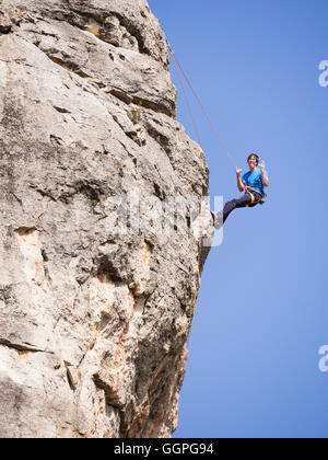 Caucasian man climbing rock gesticulant avec langue Banque D'Images