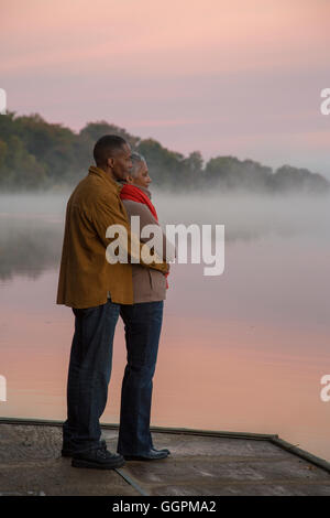 Vieux couple hugging at foggy river au lever du soleil Banque D'Images