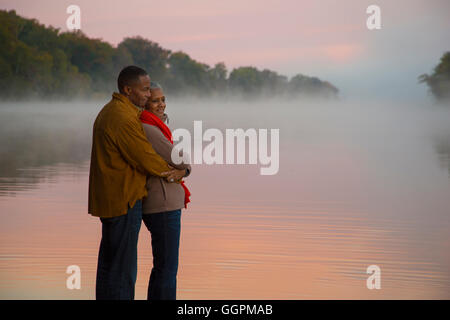 Vieux couple hugging at foggy river au lever du soleil Banque D'Images