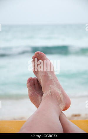 Tendue détendue jambes croisées sur un fauteuil jaune avec pieds de sable donnant sur la plage et des vagues à Riviera Maya, Mexique Banque D'Images