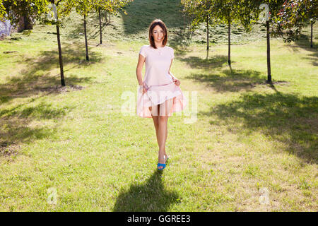 Femme dans une robe rose de promenades à travers le parc en été Banque D'Images