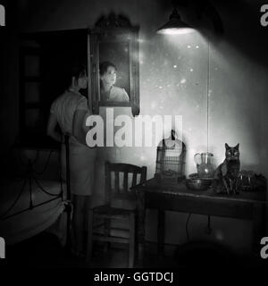 Young woman standing by le miroir dans la vieille chambre avec black cat sitting on table Banque D'Images