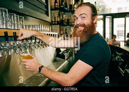 Smiling Caucasian bartender pouring beer Banque D'Images