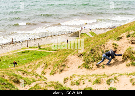 Kaseberga, Suède - août 1, 2016 : Young adult man and woman grimper une pente de la côte de sable de la mer ci-dessous. Situation de la vie réelle Banque D'Images