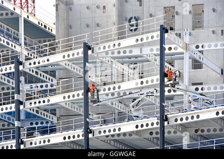 Les trous préformés de construction à ossature en acier dans les poutres facilitent l'acheminement des fixateurs en acier de service dans le travail de veste haute visibilité des cueilleurs de cerises Londres Royaume-Uni Banque D'Images