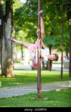 Cute girl having fun piscine en plein air à l'aide d'une lampe de rue comme un pôle de gymnastique Banque D'Images