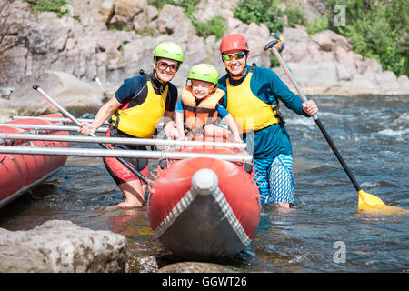 Jeune famille de trois portant des gilets et des casques qui pose à côté de catamaran aviron Banque D'Images