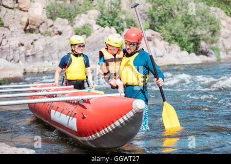 Jeune famille de trois portant des gilets et des casques d'une rangée de catamaran gonflable Banque D'Images