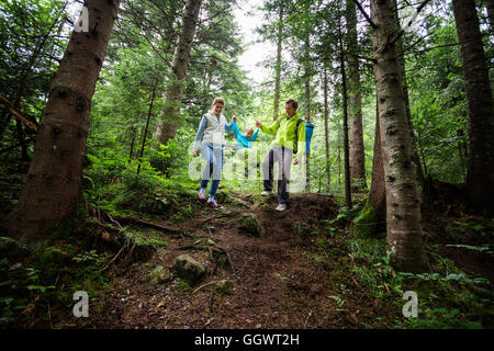 Famille de trois sur une randonnée dans une forêt de montagne. Flou de mouvement, le garçon marche dans l'air tout en tenant les mains de ses parents. Banque D'Images