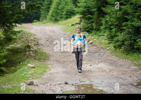 Caucasian man carrying son fils dormir dans wrap sling lors d'une randonnée Banque D'Images