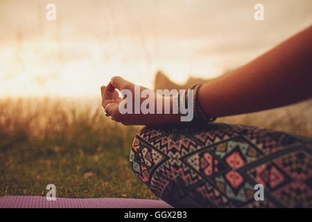 Gros plan d'une femme en posture de lotus, avec mise au point sur les mains. femme fitness méditant en plein air pendant le coucher du soleil. Banque D'Images