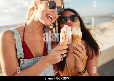 Portrait de deux jeunes femmes se tenant ensemble la consommation de crème glacée. Happy young female friends outdoor. Banque D'Images