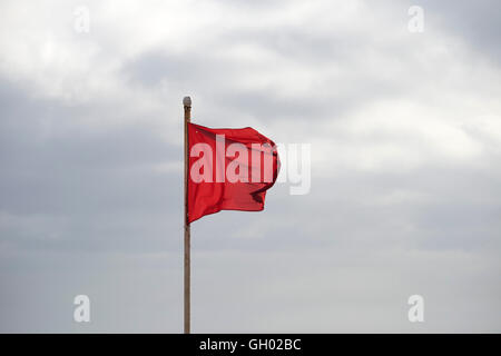 Drapeau rouge sur une plage en agitant au-dessus de ciel nuageux Banque D'Images