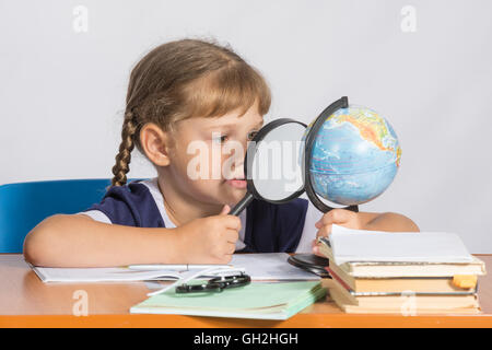 Fille de six ans assis à la table et regarde le monde à travers une loupe Banque D'Images