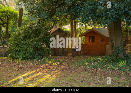 Vue automnale de cabane en bois et le Playhouse niché sous les arbres couverts de feuilles sur une pelouse dans un jardin ensoleillé, Yorkshire, Angleterre. Banque D'Images