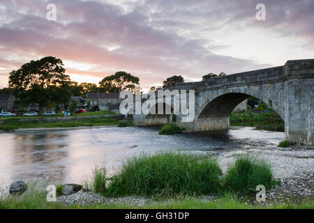 Pont en pierre enjambant la rivière Wharfe comme il coule à travers le village pittoresque de Tonbridge, dans le cadre d'été dramatique soir Ciel rouge - Vallées du Yorkshire, England, UK. Banque D'Images