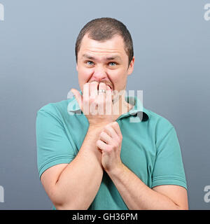 Portrait of a man biting nails et d'être effrayé à l'arrière-plan gris Banque D'Images