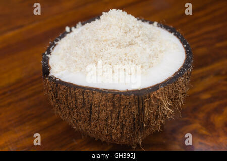 Une demi noix de coco avec de la noix de coco râpée tomber sur une table en bois. Banque D'Images