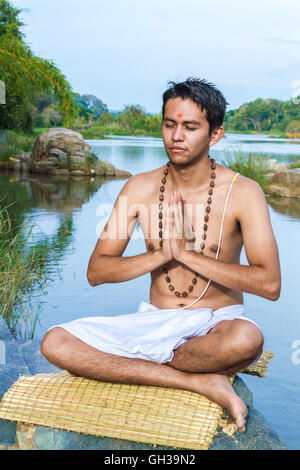 Un jeune prêtre hindou (brahmane) siège dans la prière au bord de la rivière. Banque D'Images