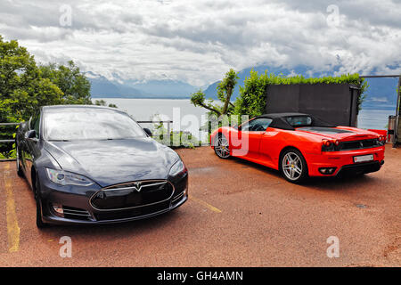 Une Tesla S Berline électrique et d'une Ferrari rouge décapotable voiture garée dans un un panorama du lac de Genève, Chebrex, Vaud, CH Banque D'Images