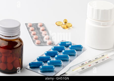 Le traitement à domicile. Thermomètre de verre et divers comprimés sous blister et bouteilles sur fond blanc Banque D'Images