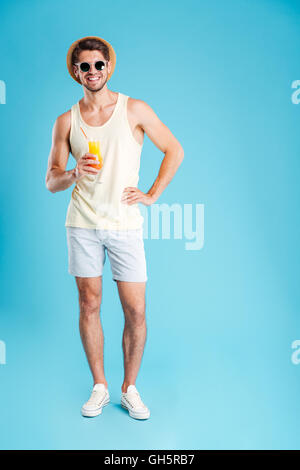 Toute la longueur de cheerful young man holding et verre de jus d'orange sur fond bleu Banque D'Images