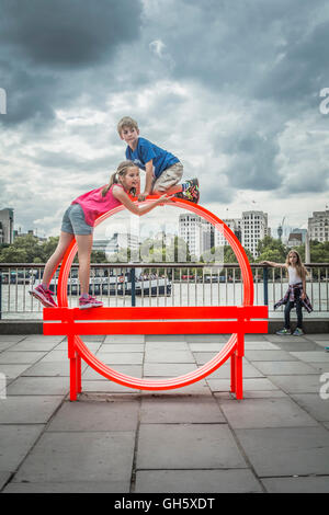 Enfants jouant sur l'un de par la modification de Jeppe Hein Bancs sociaux sur London's South Bank, SE1, UK Banque D'Images