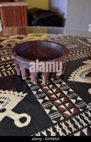 Tanoa Samoan antique ou laulau le kava bol sculpté dans du bois. Tapa Samoan chiffon sous verre sur table. Banque D'Images