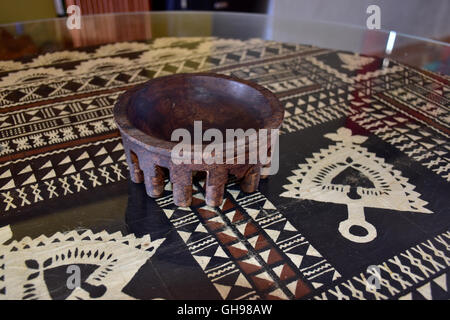 Tanoa Samoan antique ou laulau le kava bol sculpté dans du bois. Tapa Samoan chiffon sous verre sur table. Banque D'Images