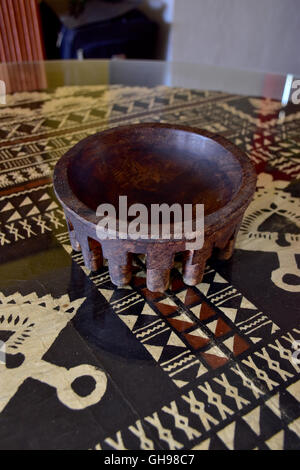 Tanoa Samoan antique ou laulau le kava bol sculpté dans du bois. Tapa Samoan chiffon sous verre sur table. Banque D'Images