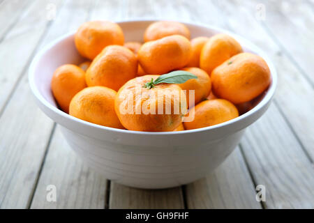 Mandarines satsuma imparfaite - produire des fruits biologiques - dans un bol blanc sur un fond de bois. Banque D'Images