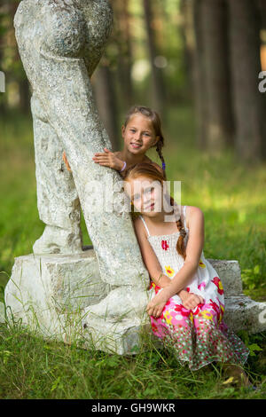 Deux mignonnes petites filles posant près de statue dans un parc. Banque D'Images