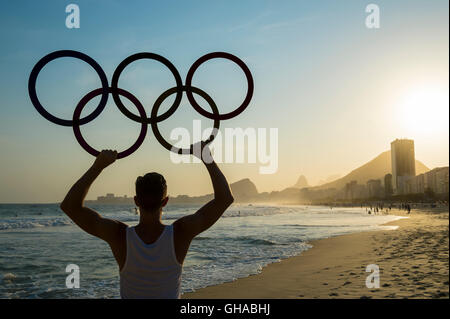 RIO DE JANEIRO - le 30 octobre 2015 : Athlète est titulaire d'anneaux olympiques au-dessus les toits de la ville au coucher du soleil sur la plage de Copacabana à partir de Leme. Banque D'Images