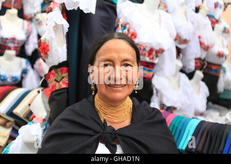 Femme plus âgée en robe traditionnel équatorien, debout en dehors de ses vêtements fait main en décrochage marché Otavalo Banque D'Images