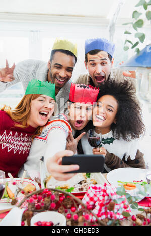 Silly amis in paper crowns en tenant au dîner de Noël selfies Banque D'Images