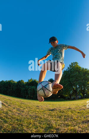 Un garçon jouant au football, l'exécution de freestyle dans un parc urbain à jouer Banque D'Images