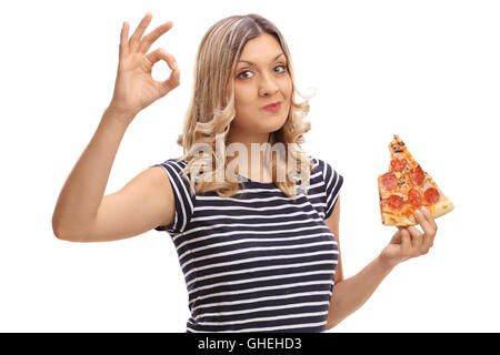 Jeune femme blonde manger une pointe de pizza et de faire un geste ok avec sa main isolé sur fond blanc Banque D'Images