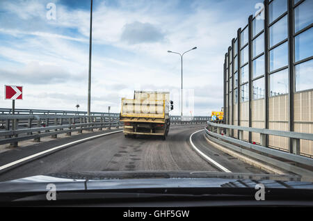 Gros camion benne industrielle va sur route asphaltée, vue arrière de cabine de voiture de tourisme Banque D'Images