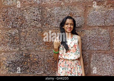 Joyeux et heureux teenage girl posing in front of gritty mur de brique rouge Banque D'Images