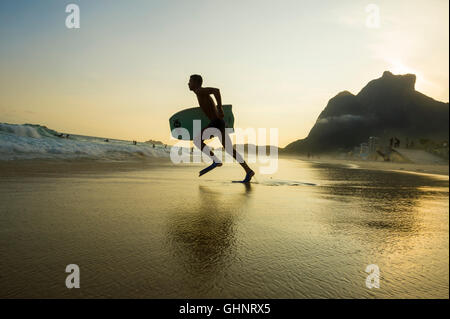 RIO DE JANEIRO - mars 8, 2016 : Bodyboarder se jette dans les vagues sur la plage de São Conrado sous un coucher de soleil silhouette. Banque D'Images