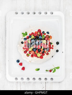 Des Pavlova gâteau avec des petits fruits frais du jardin blanc sur plaque sur fond de bois clair Banque D'Images