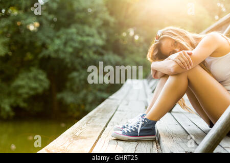 Jeune femme sportive avec de belles jambes assis sur un pont en bois garde-corps en jeans sneakers Banque D'Images