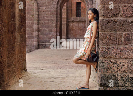 Agréable teenage Asian girl leaning against wall dans une cour du vieux bâtiment en brique. Banque D'Images