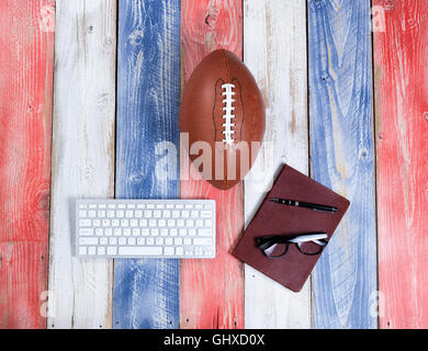 Vue de dessus de clavier d'ordinateur, lunettes de lecture, le bloc-notes, un stylo et le football américain sur le rouge, blanc et bleu les planches de bois Banque D'Images