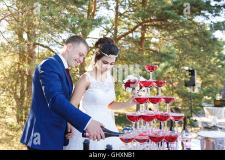 Les nouveaux mariés se verser vine dans la pyramide de verres à l'air libre le banquet de mariage Banque D'Images