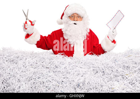 Père Noël debout dans une pile de papier déchiqueté tenant une enveloppe dans une main et une paire de ciseaux dans l'autre Banque D'Images