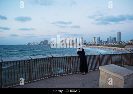 Israël, Moyen-Orient : une femme musulmane à la promenade de Jaffa après le coucher du soleil avec vue sur la mer Méditerranée et l'horizon de Tel Aviv Banque D'Images