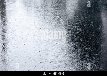 Trottoir mouillé avec des gouttes de pluie dans une flaque et réflexions Banque D'Images