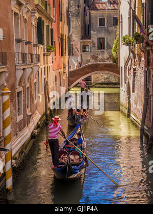 Gondolier vêtu du costume traditionnel haut rayé et chapeau canotier sa direction gondola le long d'un canal, derrière 2 autres gondoles. Venice Banque D'Images